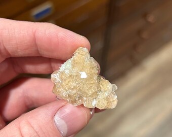 May include: A small, translucent, light golden-yellow mineral cluster featuring multiple sharp, geometric crystal points. The specimen displays a natural, multifaceted structure with a pale, crystalline texture and reflective surfaces throughout the formation.