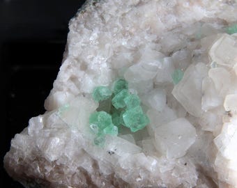 May include: Close-up of a mineral specimen featuring a matrix of white, crystalline formations. Embedded within are clusters of small, vibrant green crystals, creating a striking contrast. The overall texture is rough and natural.