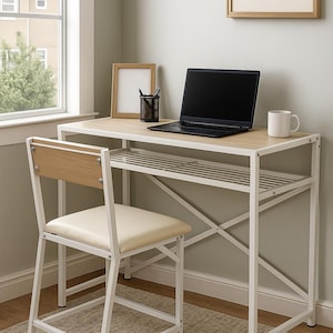 May include: A contemporary white metal desk and chair set with a light wood-effect desktop and chair back. A laptop, mug, and picture frame are on the desk. The chair has a cream-coloured seat. The desk has a lower shelf.