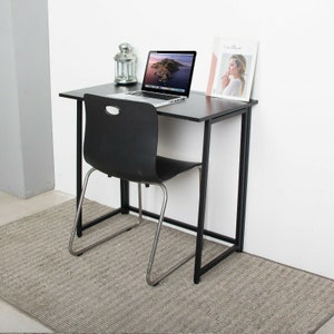 May include: A black folding desk with a black metal frame and a laptop computer on top. A black chair with a silver frame is in front of the desk. The desk is sitting on a grey rug.