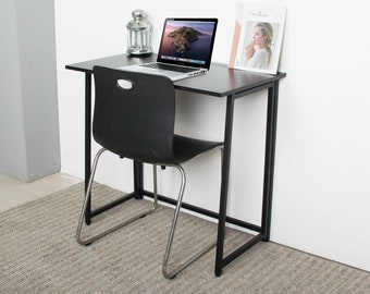 May include: A black folding desk with a black metal frame and a laptop computer on top. A black chair with a silver frame is in front of the desk. The desk is sitting on a gray rug.