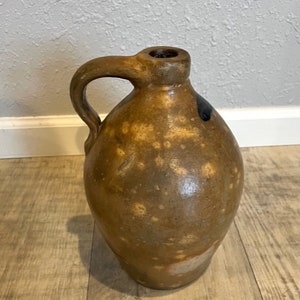 May include: A brown stoneware jug with a blue glaze and a handle. The jug has a rustic, antique look.