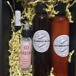 May include: A set of three glass bottles with labels. The bottles contain a body spray, lotion, and lip balm. The labels are white with black text and feature the words "Cucumber Melon" and "So Fresh".
