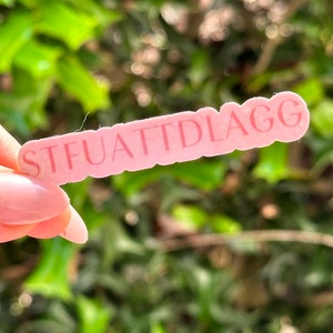 May include: Pink sticker with the text "STFUATTIDLAGG" in white lettering.