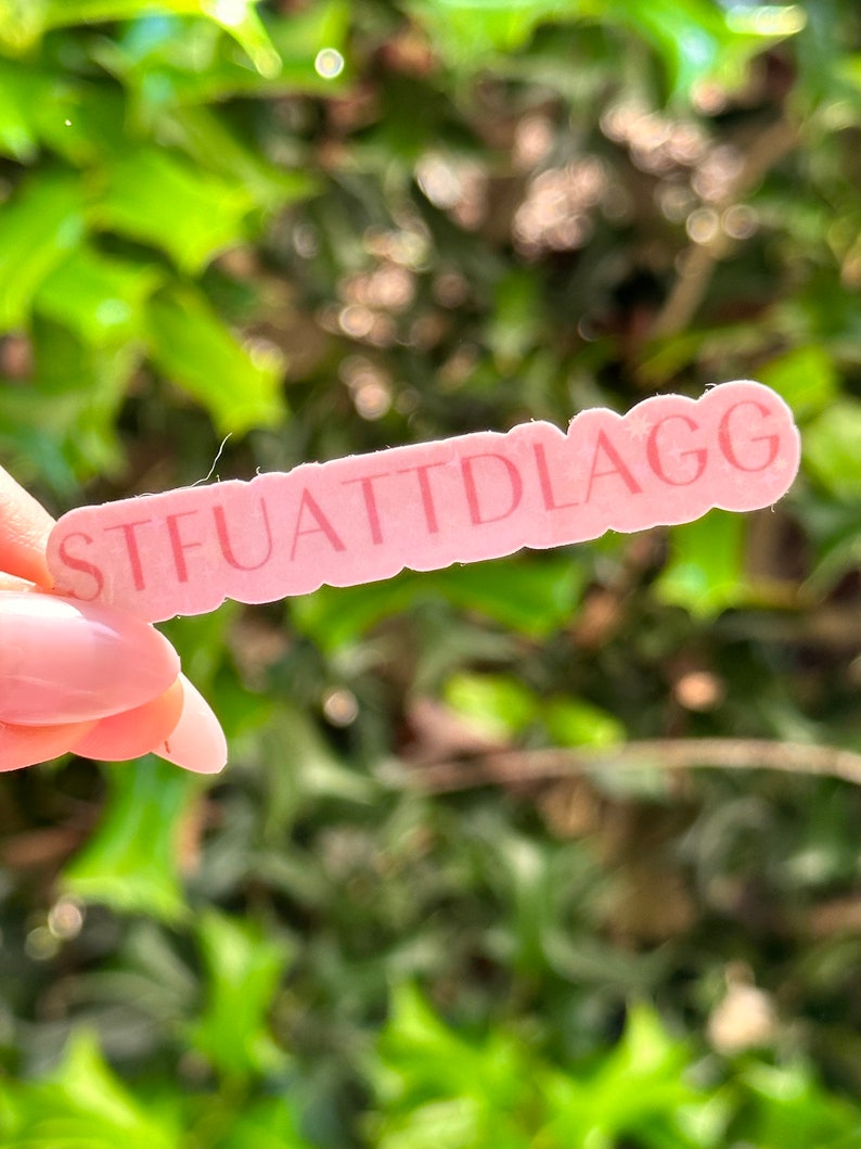 May include: Pink sticker with the text "STFUATTIDLAGG" in white lettering.