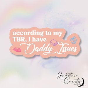 May include: A pink sticker with the text "according to my TBR, I have Daddy Issues" and three illustrated books in pink, purple, and blue.