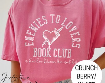 May include: Pink t-shirt with a white graphic design that says "Enemies to Lovers Book Club" with a heart pierced by a dagger. The text below the graphic says "a fine line between love and hate".