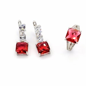 May include: A set of jewelry featuring a red square-shaped gemstone with clear cubic zirconia accents. The set includes a ring and a pair of earrings.