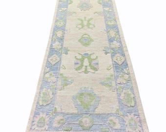 May include: A light blue and green patterned runner rug with a fringe border. The rug has a cream background with a floral design.