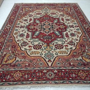 Puede incluir: Una alfombra persa tradicional con un patrón floral rojo, crema y azul. La alfombra tiene un medallón central y un borde con diseños intrincados.