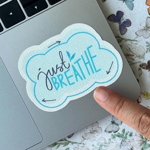 Puede incluir: Una pegatina azul y blanca con el texto "Just Breathe" en letra negra. La pegatina está en un portátil plateado.