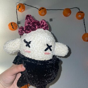 Pode incluir: Um brinquedo de pelúcia branco com um corpo de veludo preto e um mohawk de veludo bordô. O brinquedo tem X para os olhos e bochechas cor-de-rosa.