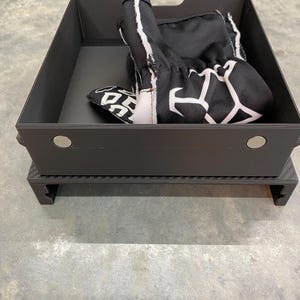May include: A black storage box with a black and white patterned glove inside. The box has a carbon fiber base.