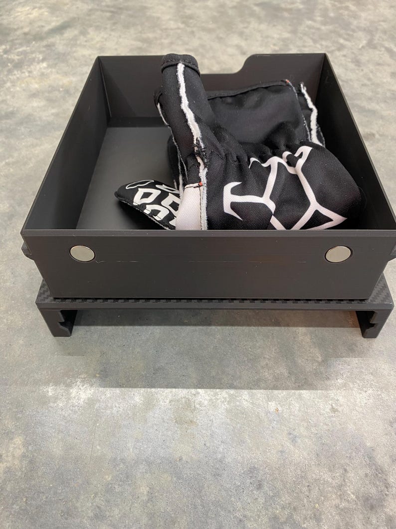 May include: A black storage box with a black and white patterned glove inside. The box has a carbon fiber base.