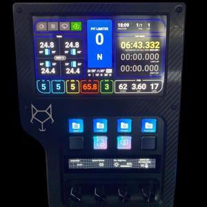 Puede incluir: Panel de instrumentos de carreras negro con textura de fibra de carbono. La pantalla muestra los tiempos por vuelta, las temperaturas y los niveles de combustible. Tiene varios botones y una pantalla que muestra información en blanco, azul y verde.