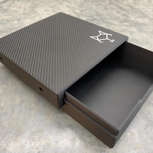 May include: A black drawer with a carbon fiber top and a white wolf logo. The drawer is open and the inside is black.