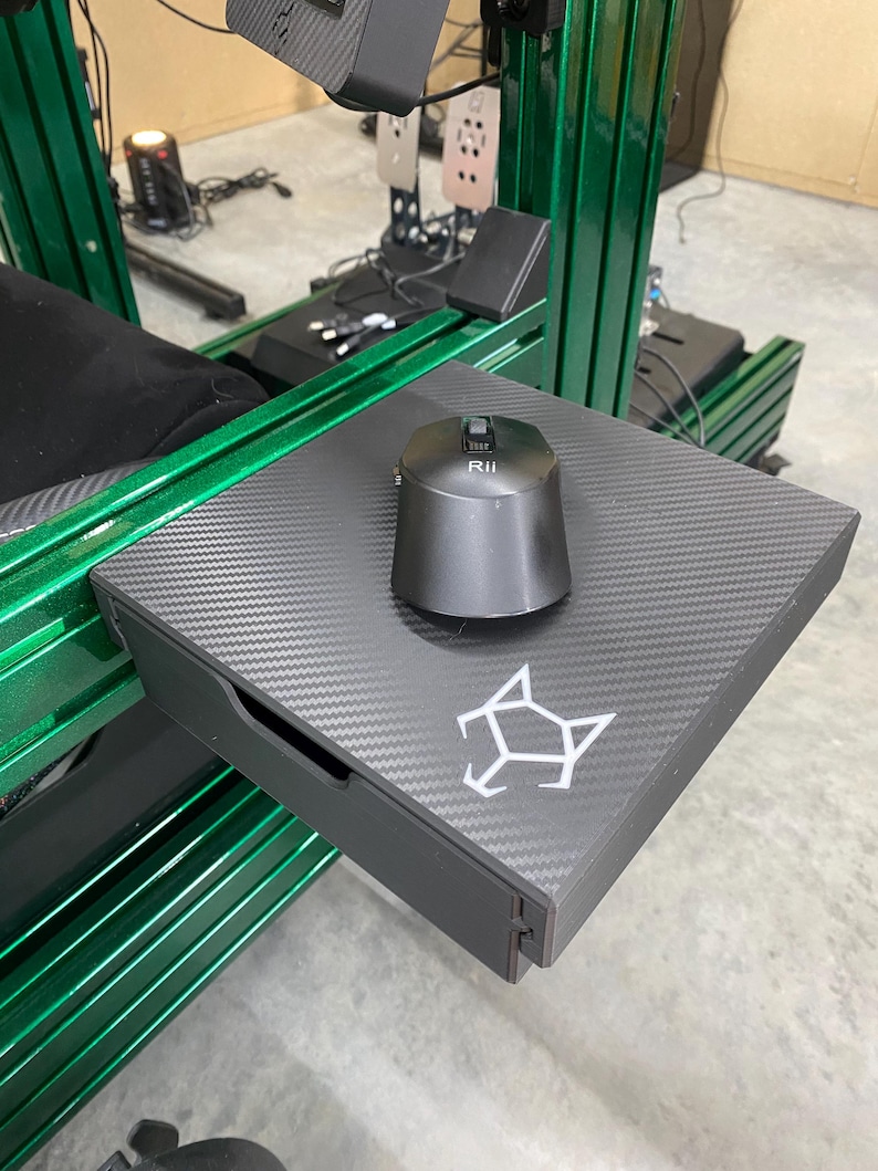 May include: A black carbon fiber tray with a drawer and a black mouse with a button labeled "RII". The tray is mounted on a green metal frame.