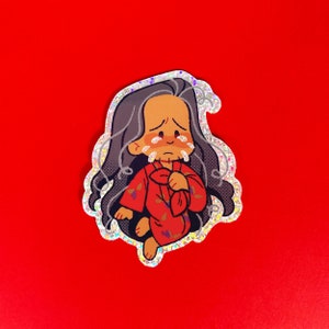 Puede incluir: Una pegatina holográfica con una ilustración de dibujos animados de una figura llorando con un atuendo rojo. La figura tiene pelo largo gris y está derramando lágrimas. La pegatina tiene un borde brillante e iridiscente y está sobre un fondo rojo.