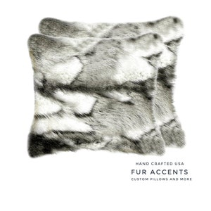 Könnte beinhalten: Zwei quadratische Zierkissen mit Kunstfellstruktur in Grau- und Weißtönen. Die Kissen werden auf weißem Hintergrund präsentiert. Der Text "FUR ACCENTS" und "CUSTOM PILLOWS AND MORE" ist sichtbar.
