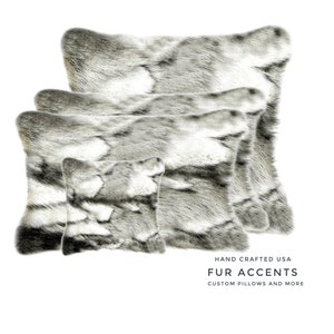 May include: Four different sizes of grey and white faux fur throw cushions. The cushions are arranged in a pyramid shape with the largest cushion at the top and the smallest cushion at the bottom. The cushions are all made of soft, plush fur and have a luxurious feel. The text "HAND CRAFTED USA FUR ACCENTS CUSTOM PILLOWS AND MORE" is printed below the cushions.