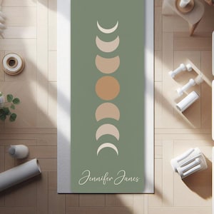 May include: A green yoga mat with a design of a crescent moon in various phases. The mat has the name "Jennifer Janes" printed on the bottom.