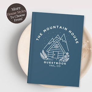 May include: A navy blue guestbook with the text "THE MOUNTAIN HOUSE GUESTBOOK VAIL, CO" in white. The cover features a cabin illustration with mountains and floral accents. A circular graphic reads "More House Styles To Choose From!"
