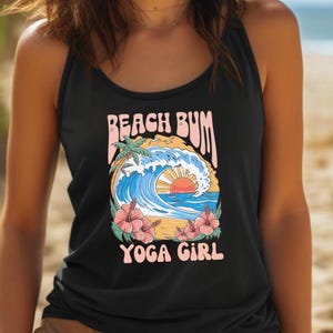 May include: Black tank top with a colorful graphic featuring a wave, palm tree, and sunset, with the words "Beach Bum Yoga Girl". The woman is smiling on a sandy beach.