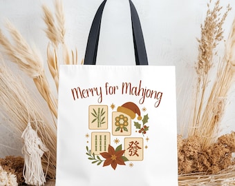 May include: White tote bag with black handles featuring the text "Merry for Mahjong" in brown. The design includes Mahjong tiles, a Santa hat, holly, and a poinsettia. The bag is made of a sturdy material.