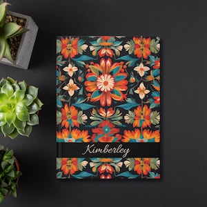 May include: A black notebook with a colorful floral pattern and a black band with the name "Kimberly" printed in white.
