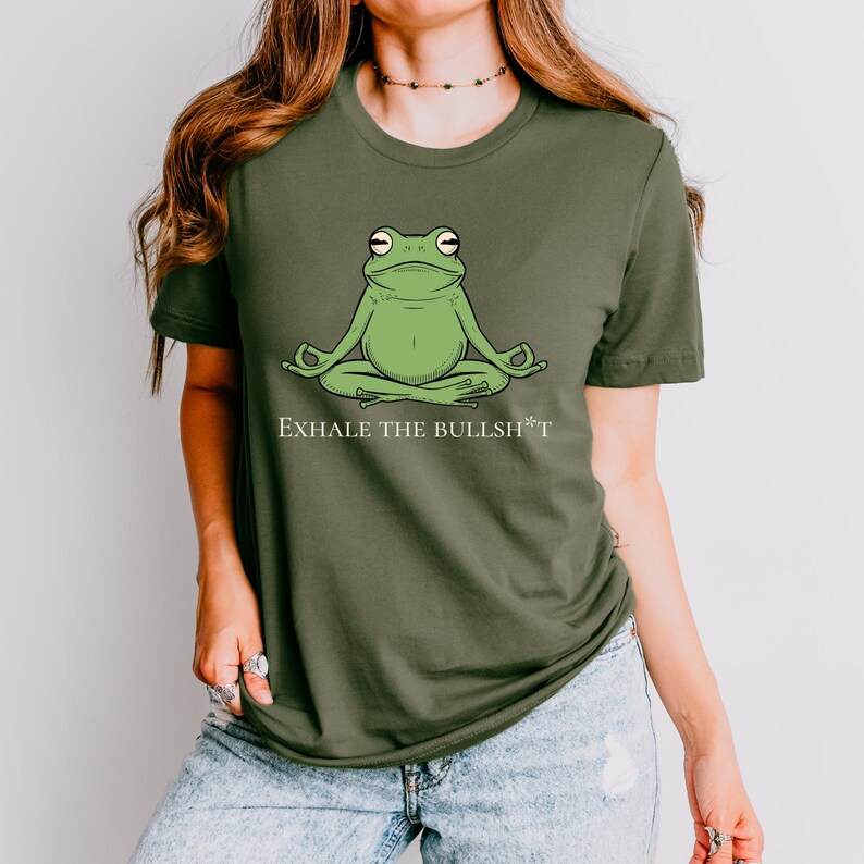 May include: A green t-shirt with a graphic of a green frog sitting in a yoga pose. The text "Exhale the Bullsh*t" is printed below the frog.