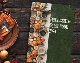 May include: A green guest book with the text "Friendsgiving Guest Book 2024" on the cover. The cover features a photo of a table setting with pumpkins, gourds, and fall foliage.