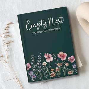 May include: A dark green journal with the words "Empty Nest" and "The Next Chapter Begins" in white script. The bottom of the journal features a watercolor floral design with pink, purple, and orange flowers.