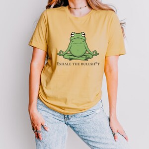 May include: A yellow t-shirt with a green frog meditating and the text "Exhale the Bullsh*t" printed on the front.