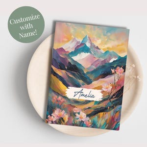 May include: A personalized notebook with a colorful mountain landscape and pink flowers. The name "Amelia" is written in blue cursive on the cover.