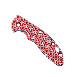 May include: Red and white patterned knife handle with a geometric design. The handle has a curved shape and several holes.