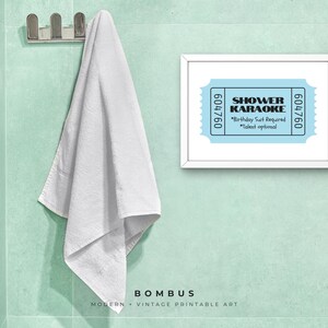 May include: A framed print with the words "SHOWER KARAOKE" on a light blue background. The print also includes the text "Birthday Suit Required" and "Talent optional". A white towel hangs on a chrome hook on a light green wall.