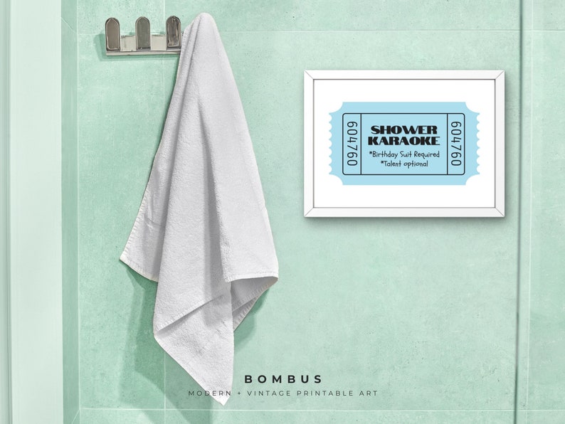 May include: A framed print with the words "SHOWER KARAOKE" on a light blue background. The print also includes the text "Birthday Suit Required" and "Talent optional". A white towel hangs on a chrome hook on a light green wall.