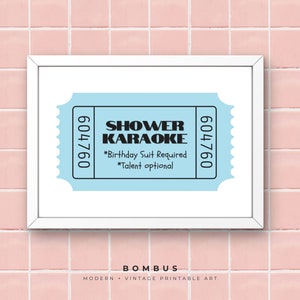 May include: A framed print with a light blue ticket design, displaying "SHOWER KARAOKE." The ticket includes the text "*Birthday Suit Required *Talent optional" and the numbers "604760." The print is set against a pink tile background.