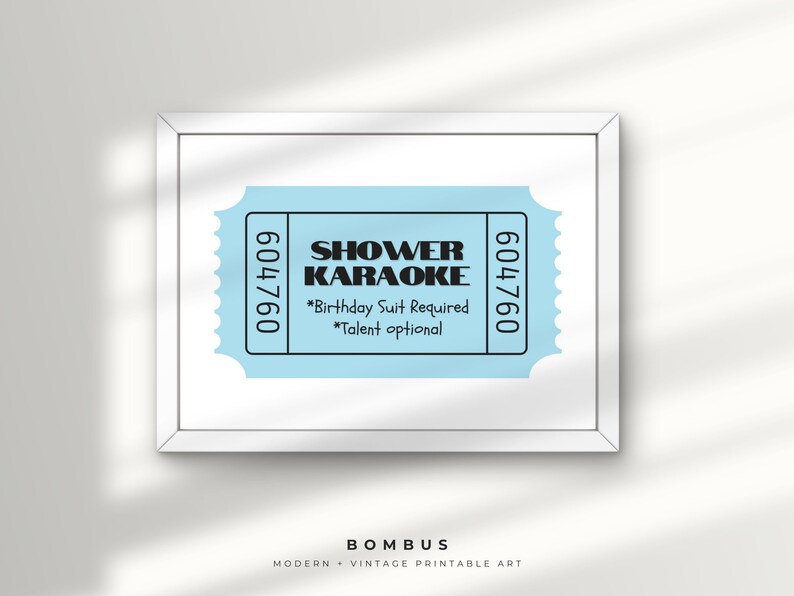 May include: A framed print with a light blue ticket design, displaying the words "SHOWER KARAOKE" in black. The ticket includes the text "*Birthday Suit Required *Talent optional" and the numbers "604760". The print is labeled "BOMBUS MODERN + VINTAGE PRINTABLE ART".