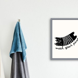 Op de afbeelding: Zwart-witte illustratie van een kat met de tekst "wash your paws" in een grijs kader.