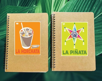 May include: Two brown notebooks with colorful stickers. The left notebook has a sticker of a glass of horchata with the text "LA HORCHATA" and the number "18". The right notebook has a sticker of a colorful pinata with the text "LA PIÑATA" and the number "17".