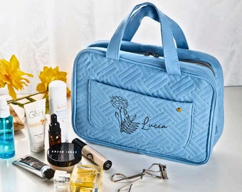 May include: A light blue quilted travel makeup bag with a zipper closure and a front pocket. The bag has a floral design and the name "Lucia" embroidered on the front.
