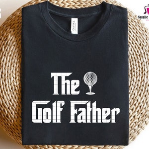 K&ouml;nnte beinhalten: Schwarzes T-Shirt mit wei&szlig;em Text "The Golf Father" und einer Grafik mit Golfball und Tee.