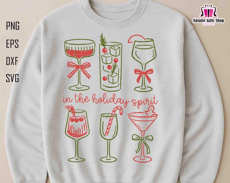 May include: A light gray sweatshirt featuring a festive design with six cocktail glasses in red and green. The phrase "in the holiday spirit" is printed below the glasses. The design includes a bow, candy cane, and gingerbread man.