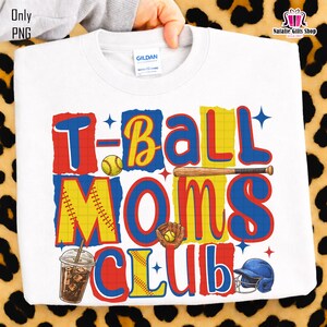 May include: White sweatshirt with the text "T-Ball Moms Club" in red, yellow, and blue. The design includes baseball-themed graphics such as a baseball, bat, glove, helmet, and a drink. The sweatshirt is held by a hand.