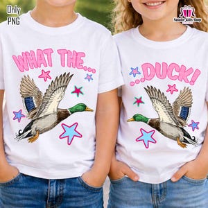 May include: Two white t-shirts with the phrases "WHAT THE..." and "DUCK!" in pink, each featuring a cartoon duck with green heads, blue and brown wings, and blue and pink stars. The shirts are worn by children.