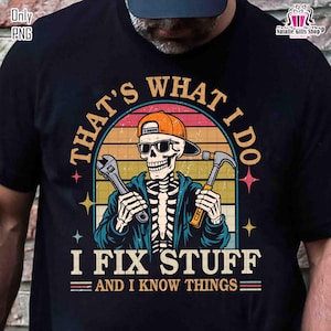 Puede incluir: Camiseta negra con un diseño de esqueleto con gafas de sol y gorra naranja, sosteniendo una llave inglesa y un martillo. El texto dice "THAT'S WHAT I DO, I FIX STUFF, AND I KNOW THINGS" en estilo retro.