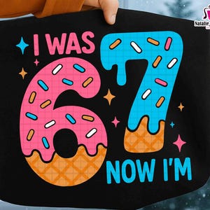 May include: Black tote bag with the text "I WAS 67 NOW I'M" in a colorful, playful design. The number 6 is designed as a pink donut with blue sprinkles, and the number 7 is blue with orange sprinkles. The bag is held by a hand.