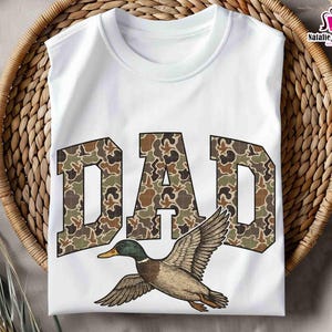 May include: White t-shirt with the word "DAD" in camouflage print and a flying duck graphic.