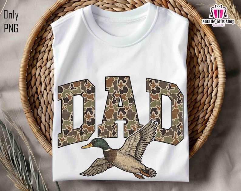 May include: White t-shirt with the word "DAD" in camouflage print and a flying duck graphic.